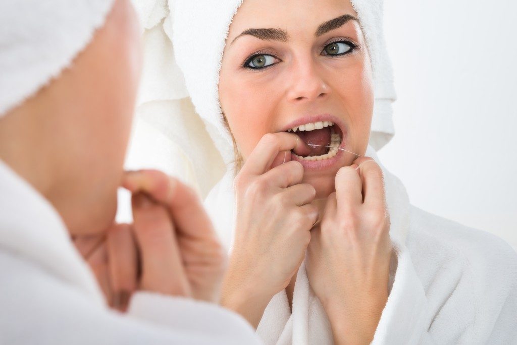 Woman looking in the mirror while flossing teeth