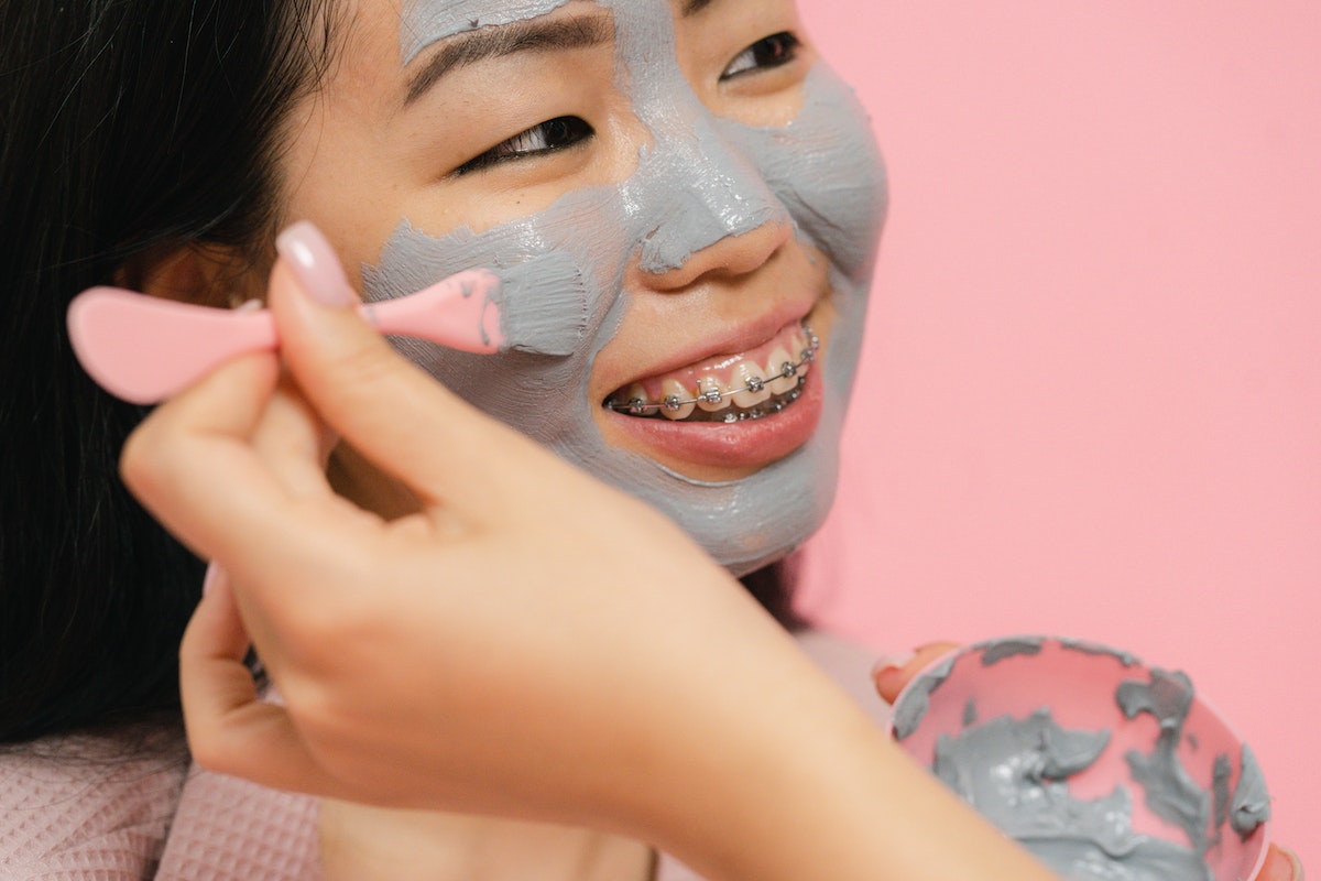 Womans hand putting cosmetic clay mask with brush on other womans face