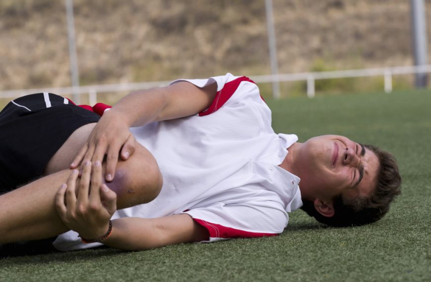 a male football player holding bruised knee in the field