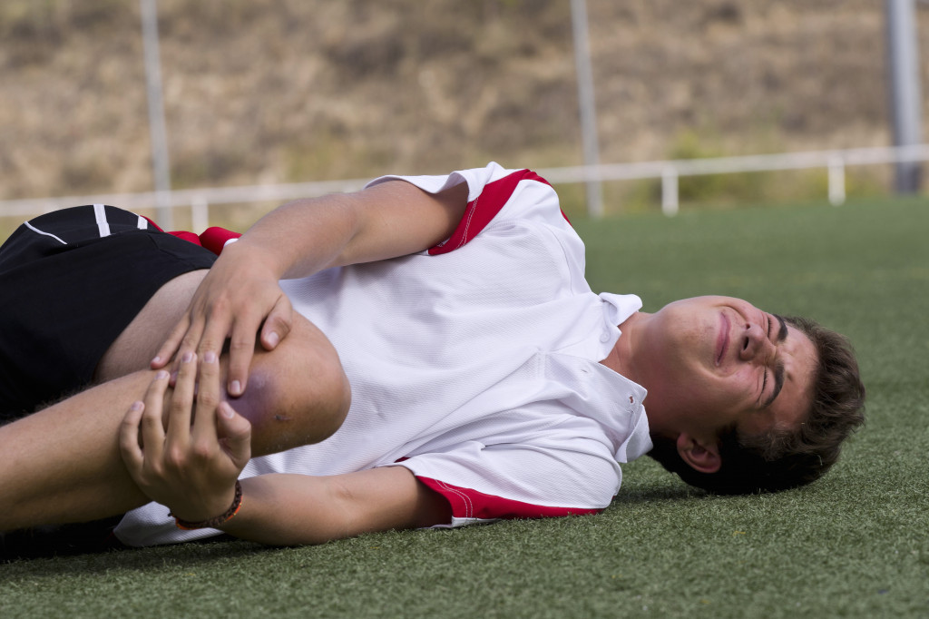 a male football player holding bruised knee in the field